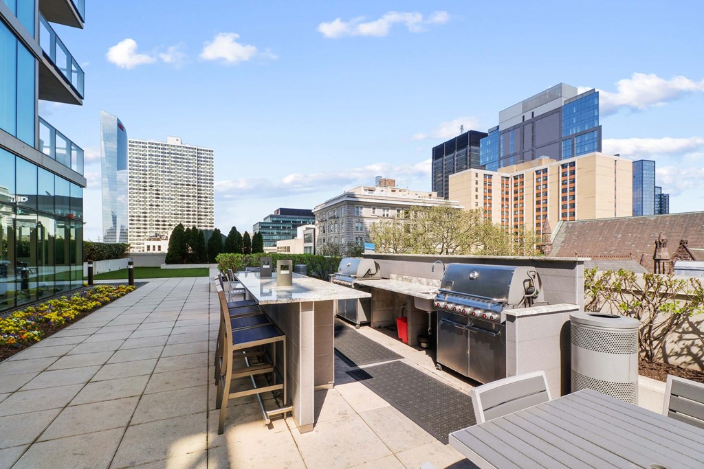 A patio with a grill and chairs overlooks a city skyline.