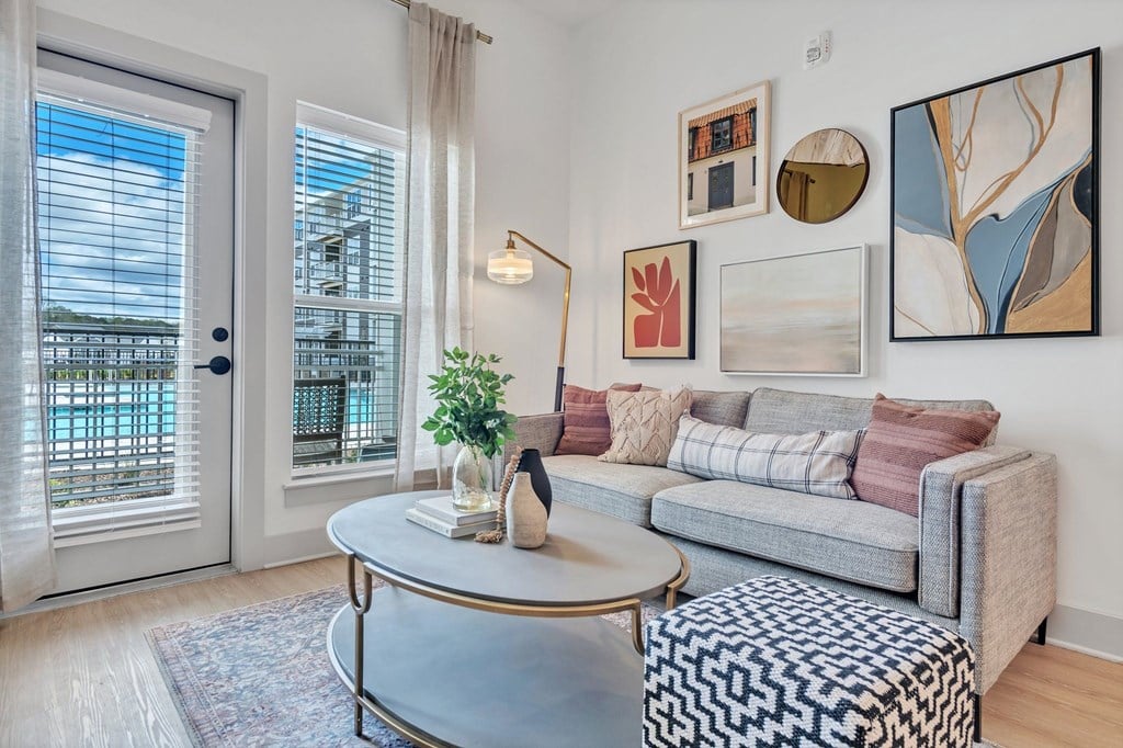A living room with a grey couch, a round table, and a painting on the wall.