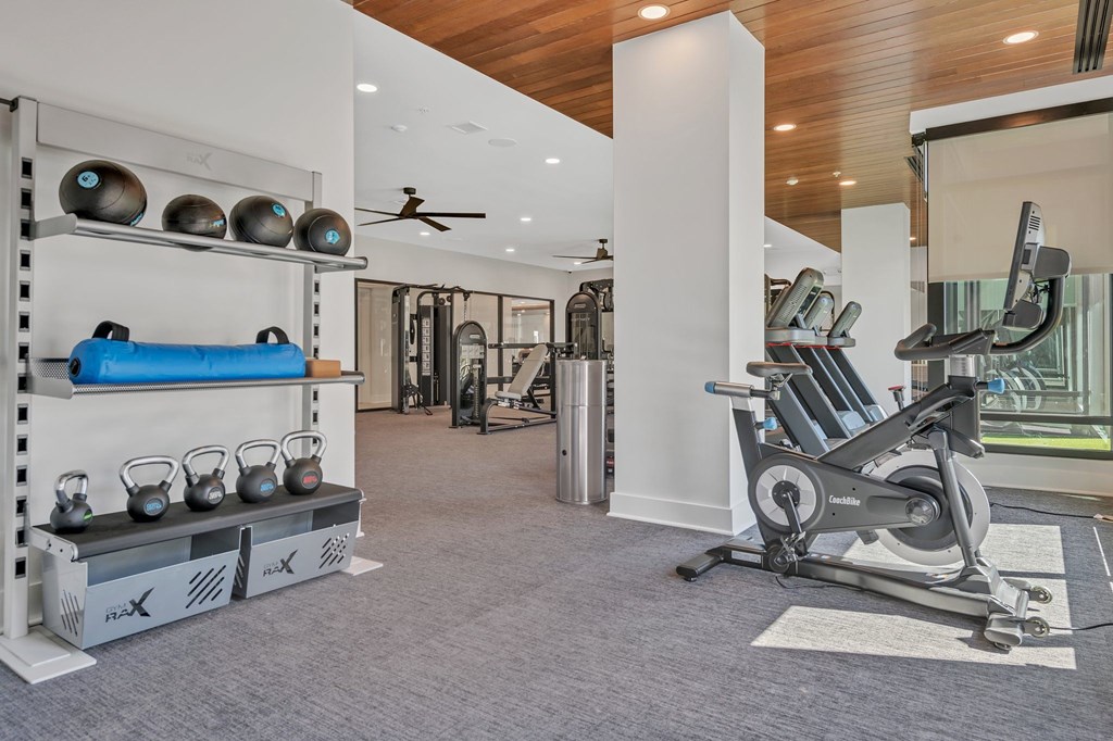 A home gym with a variety of equipment including a rowing machine, kettlebells, and a bench with a foam roller.
