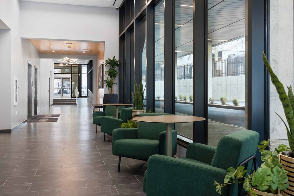 A long hallway with green chairs and a table with a plant on it.