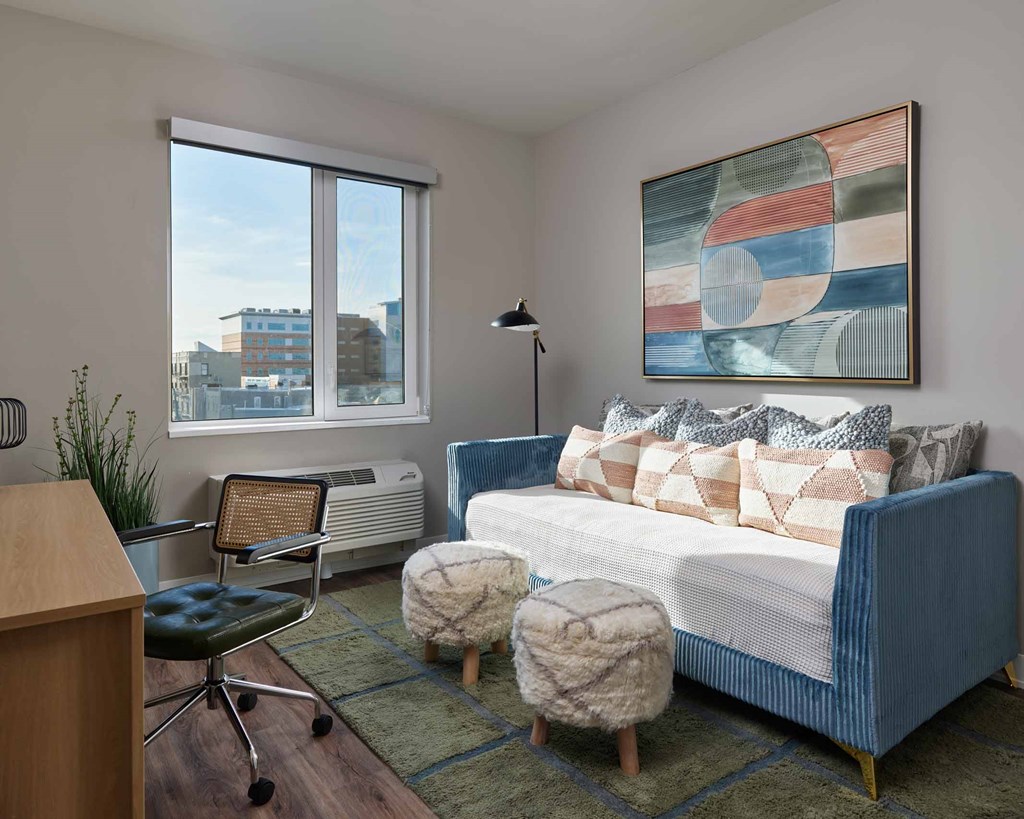A living room with a blue couch, a chair, a table, and a painting on the wall.