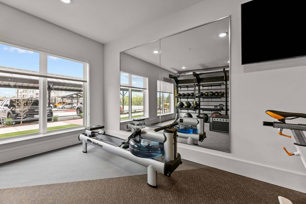 A room with a rowing machine and a mirror on the wall.