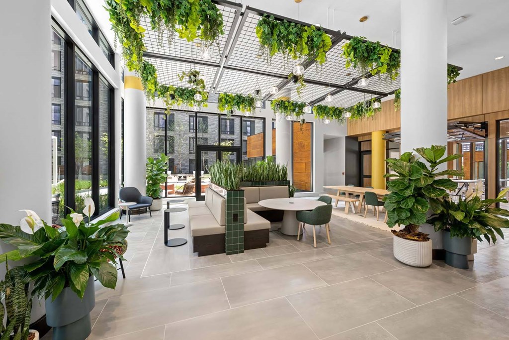A modern indoor space with a glass ceiling, white pillars, and a variety of green plants.