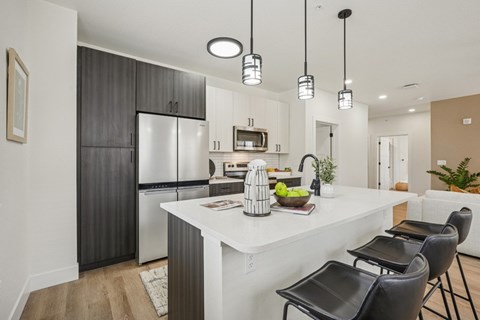 A modern kitchen with a white island and black chairs.