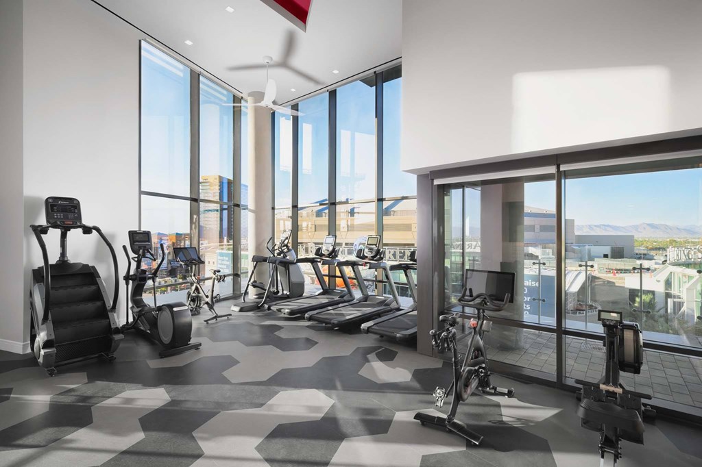 A gym with a variety of exercise equipment and a view of the city outside the windows.