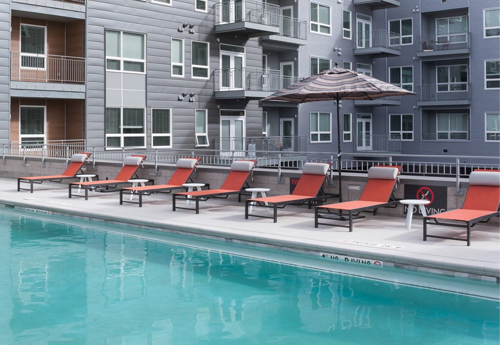 A pool with red sun loungers and a building in the background.