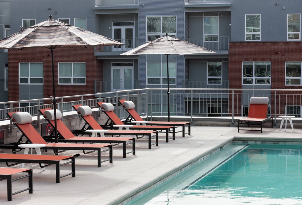 A pool area with red chairs and umbrellas.
