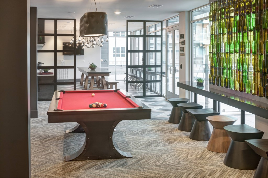 A pool table is in the middle of a room with a bar and a row of stools.