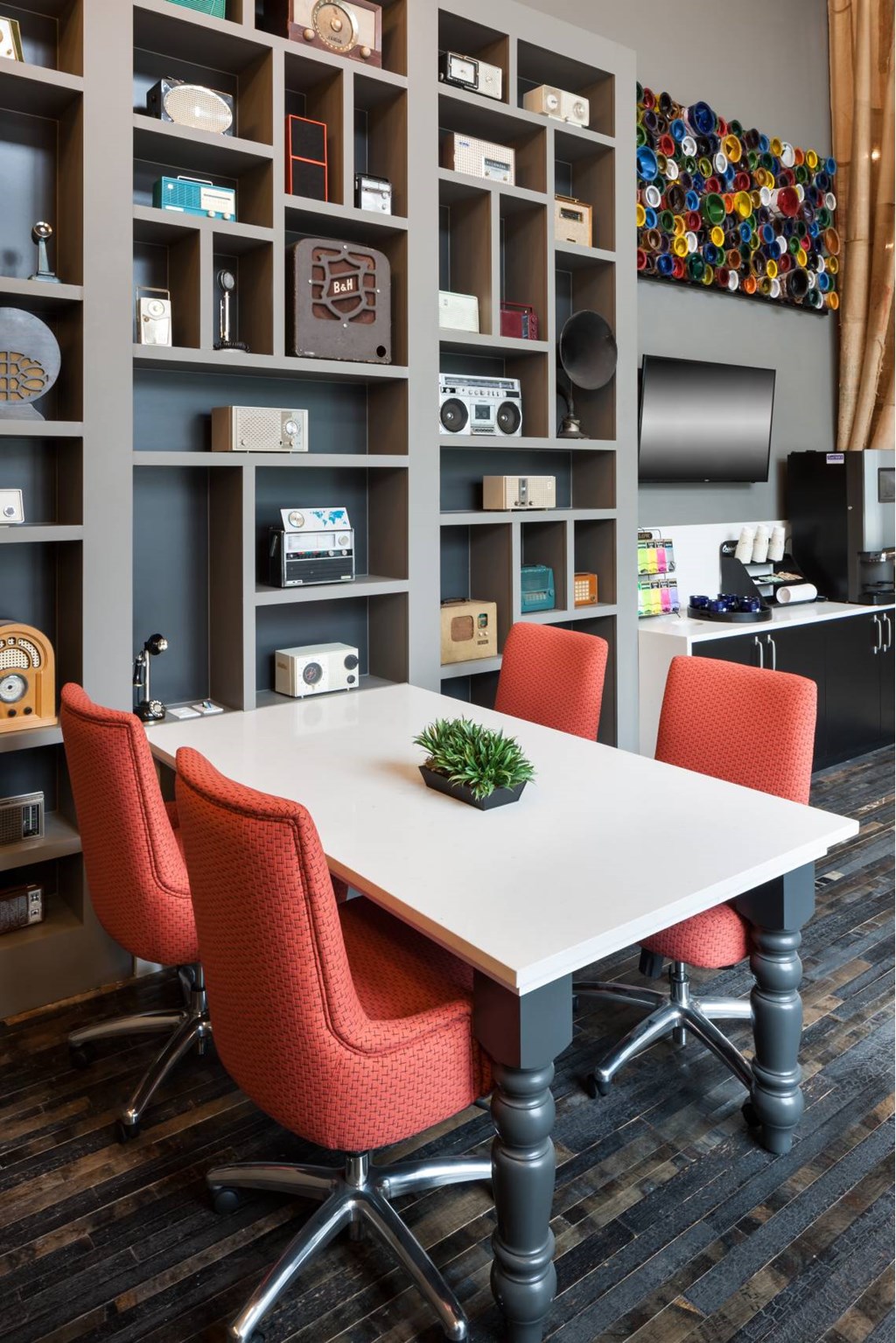 A white table with red chairs in front of a grey shelving unit.