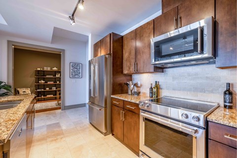 A kitchen with a stainless steel refrigerator and oven, wooden cabinets, and a marble countertop.