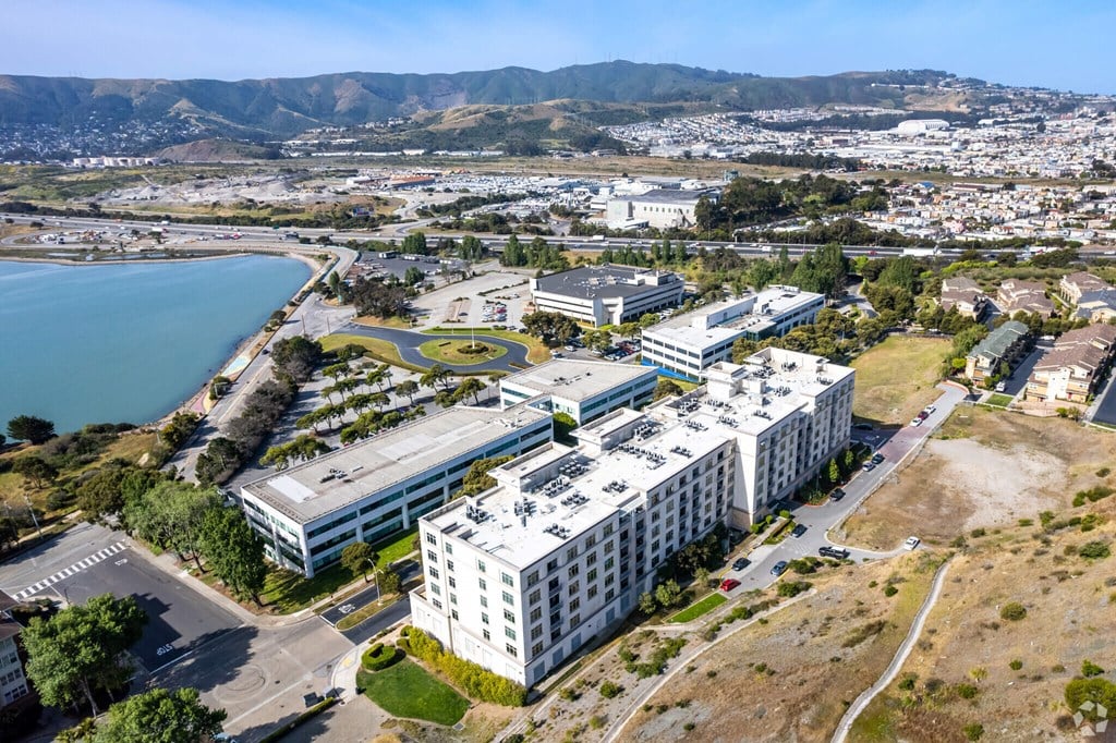 A large white building with a circular courtyard in the middle is surrounded by a parking lot and other buildings.