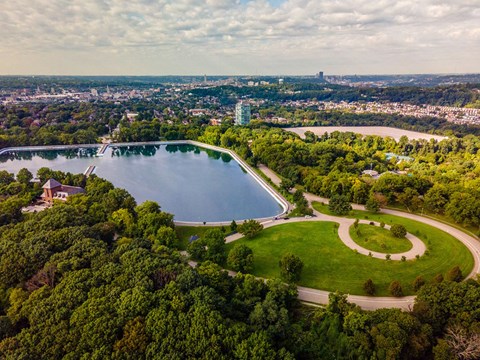 A large lake surrounded by trees and a city in the distance.
