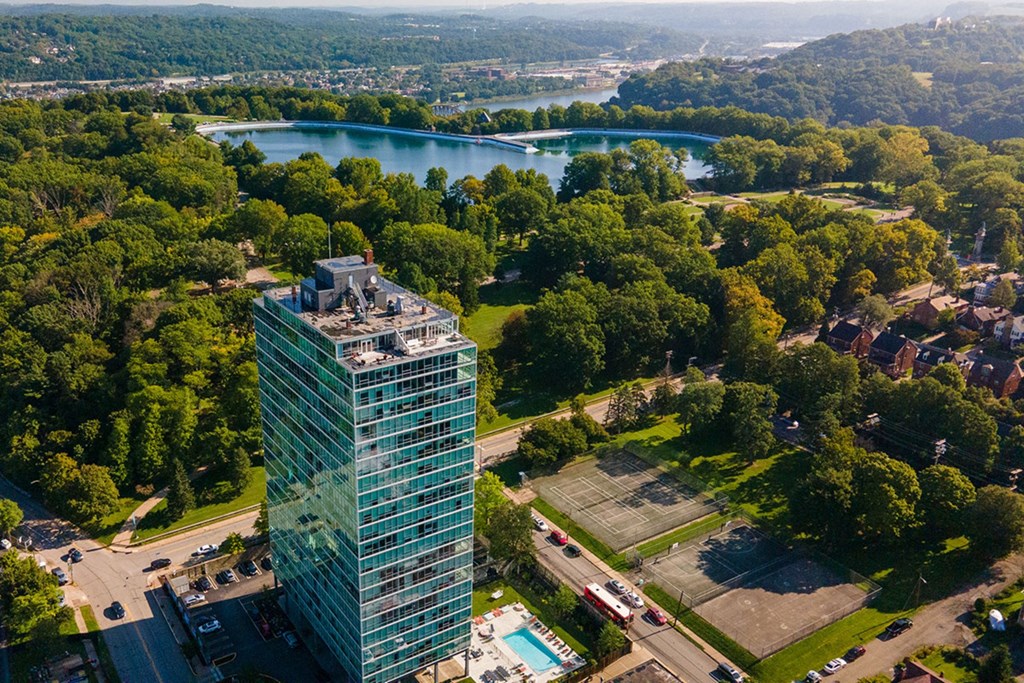 A glass building is surrounded by trees and a pool.