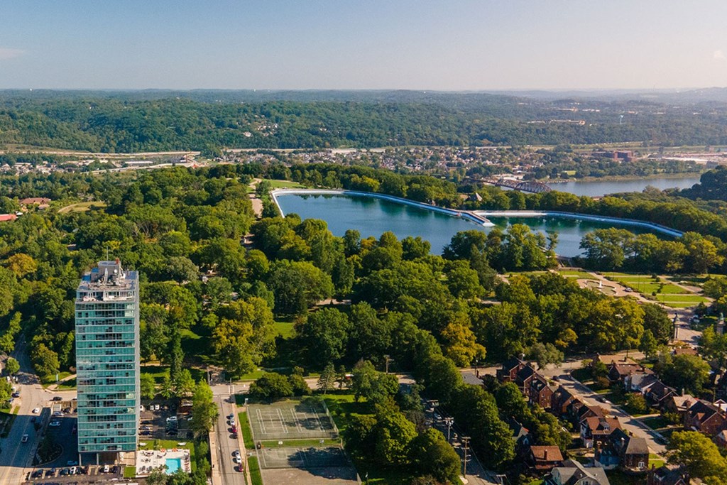 A tall glass building stands in a green landscape with a lake and a bridge in the background.