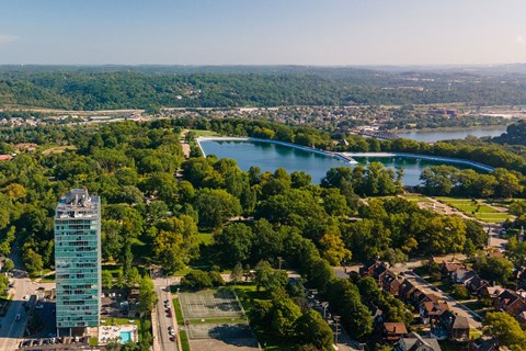 A tall glass building stands in a green landscape with a lake and a bridge in the background.