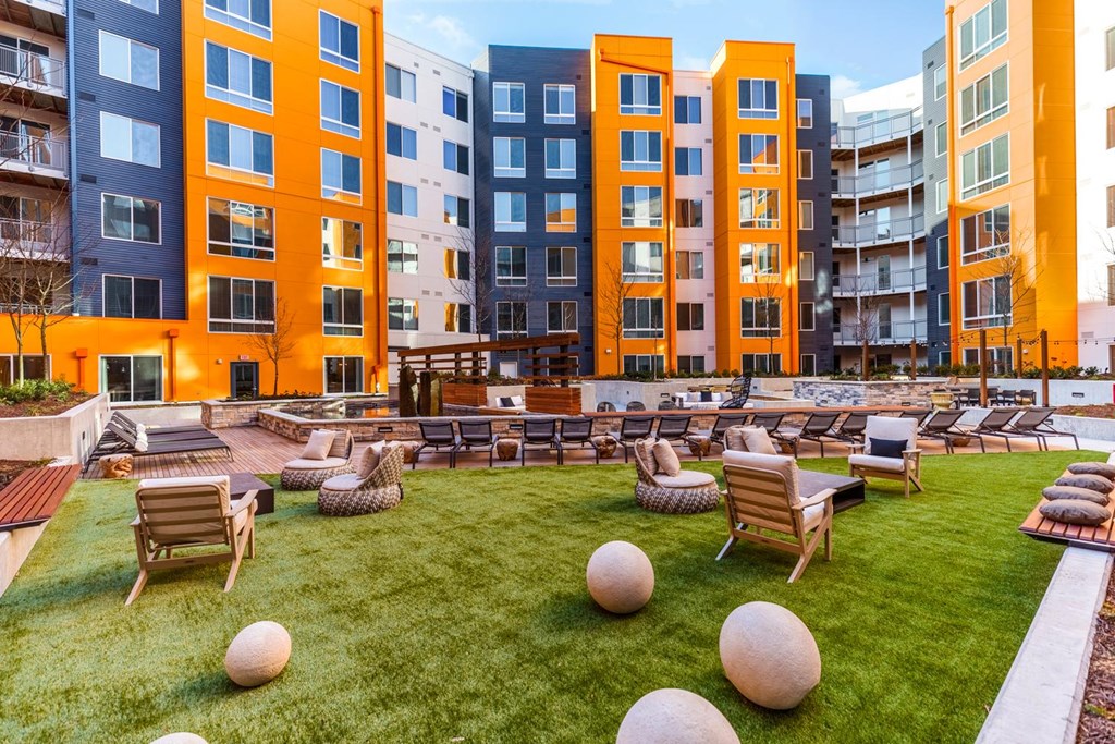 A large grassy area with chairs and bean bag chairs in front of apartment buildings.