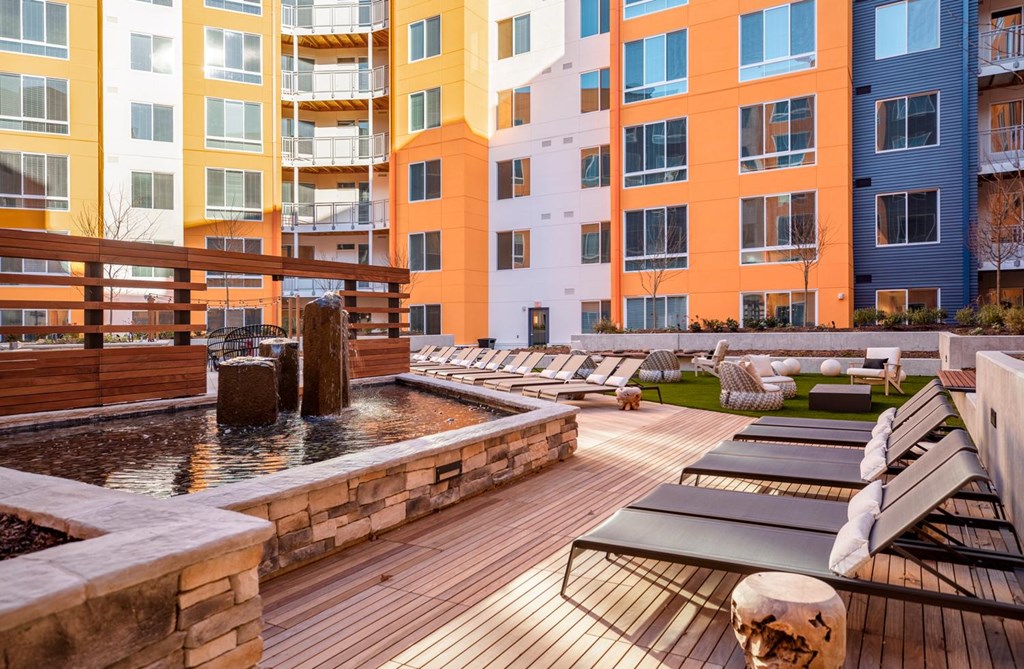 A wooden deck with benches and a water feature in front of apartment buildings.