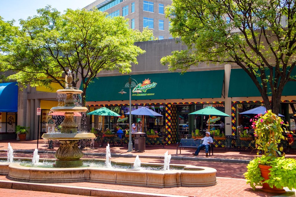 A fountain in the middle of a plaza with a man sitting on a bench.