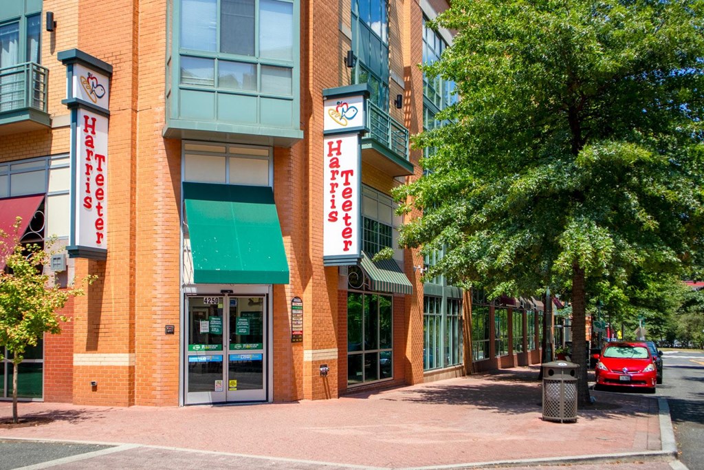 A red car is parked on the street in front of a building with a green awning.