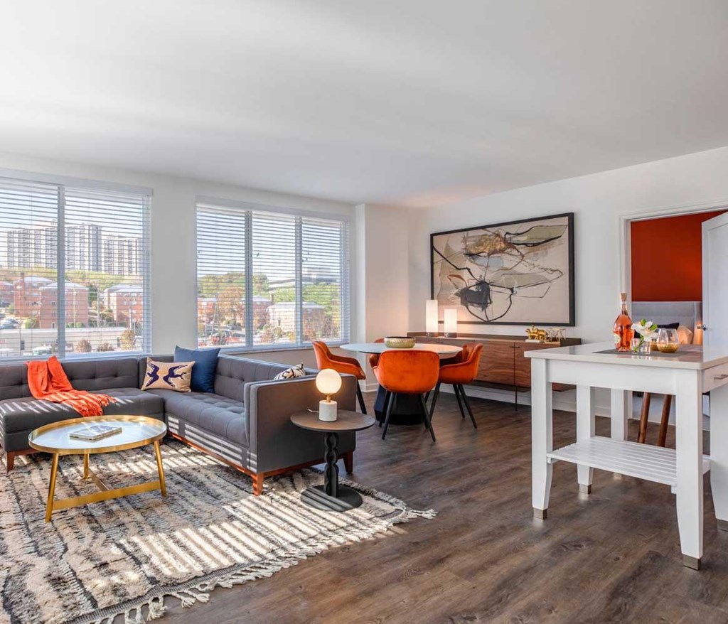 A modern living room with a grey sofa, orange chairs, and a white dining table.