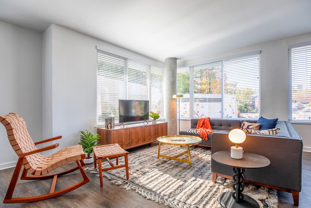 A living room with a wooden rocking chair, a grey sofa, a wooden coffee table, and a small potted plant.