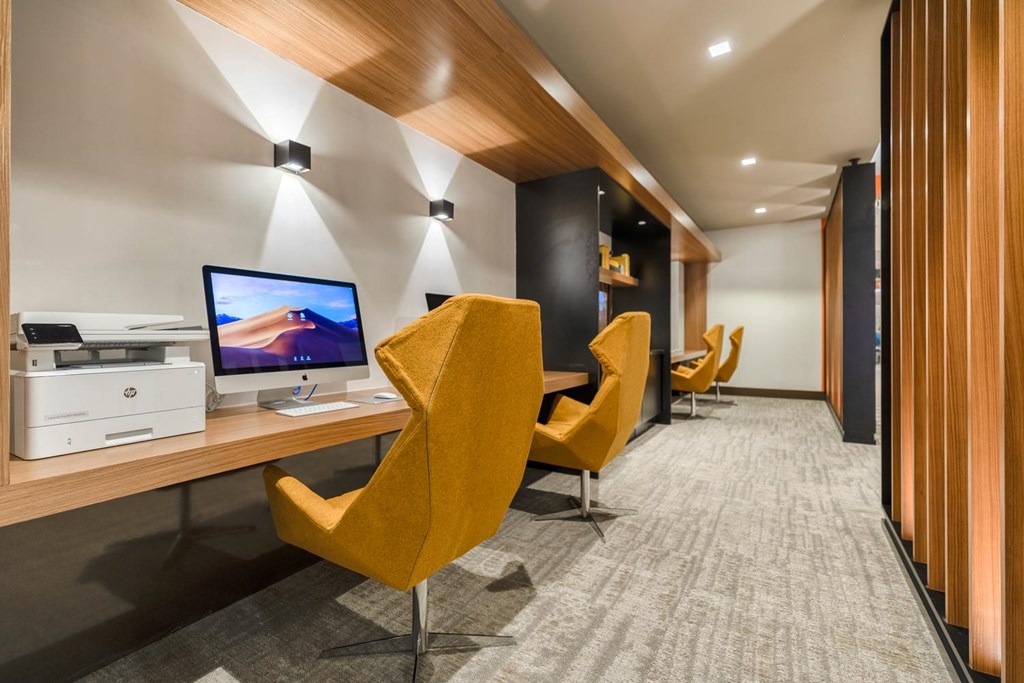 A yellow chair is in the foreground of a room with a computer on a desk.