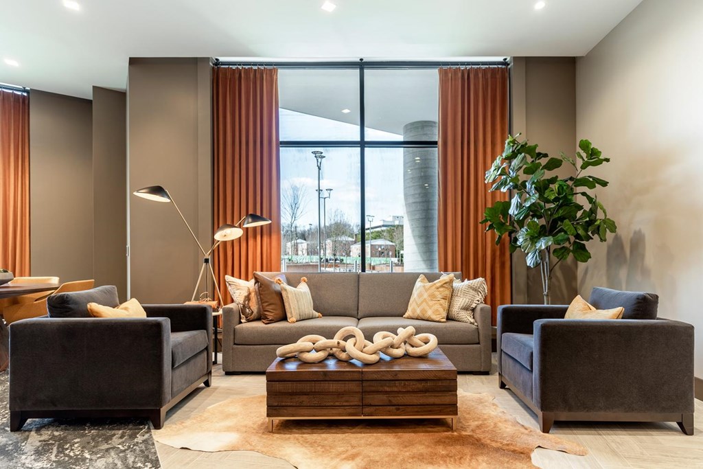 A living room with a grey couch, a brown coffee table, and a large window with orange curtains.