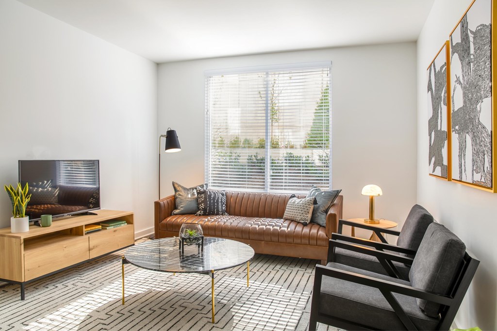 A living room with a brown couch, a glass table, and a television.