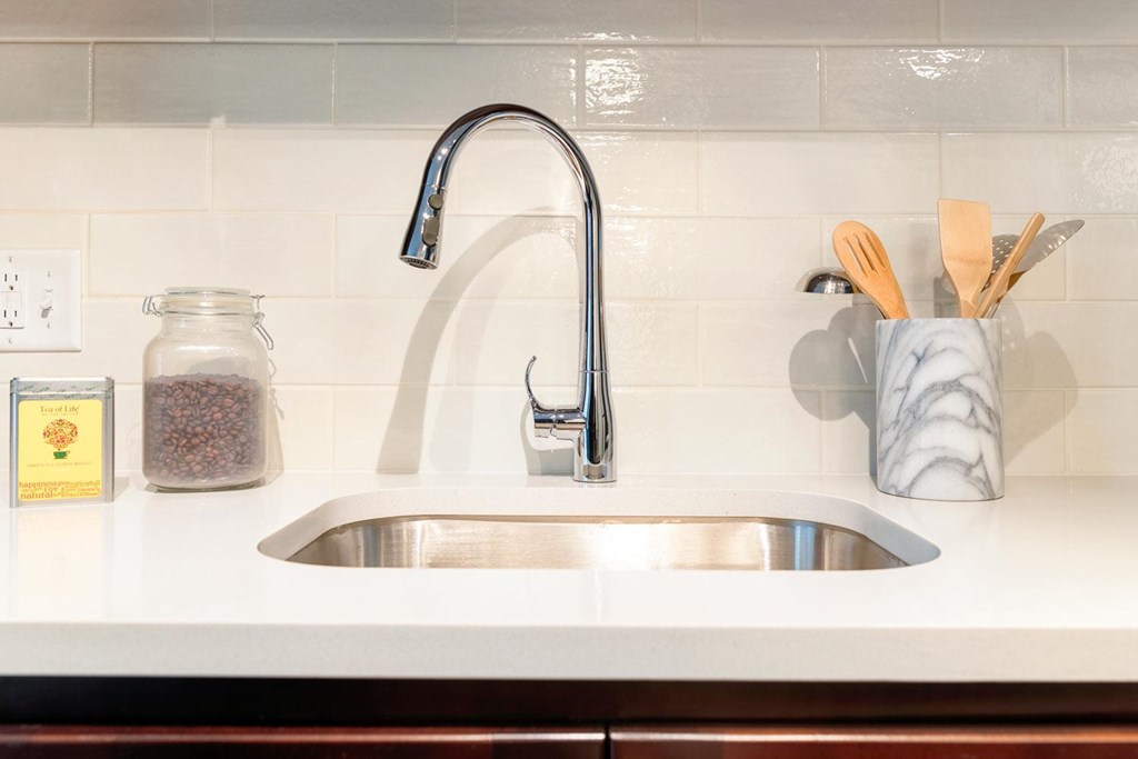 A kitchen sink with a silver faucet and a jar of spices on the counter.