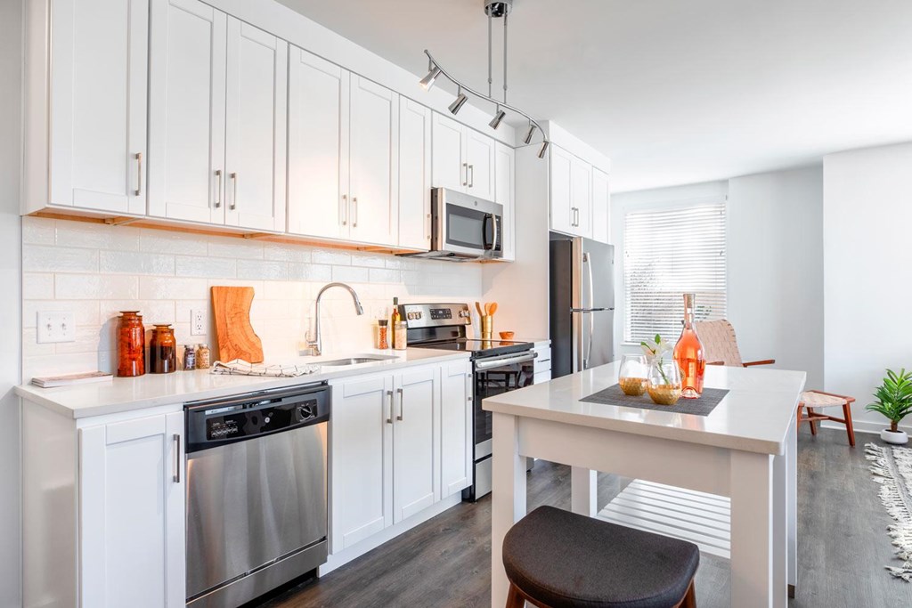 A kitchen with white cabinets and a white island with a black stool.