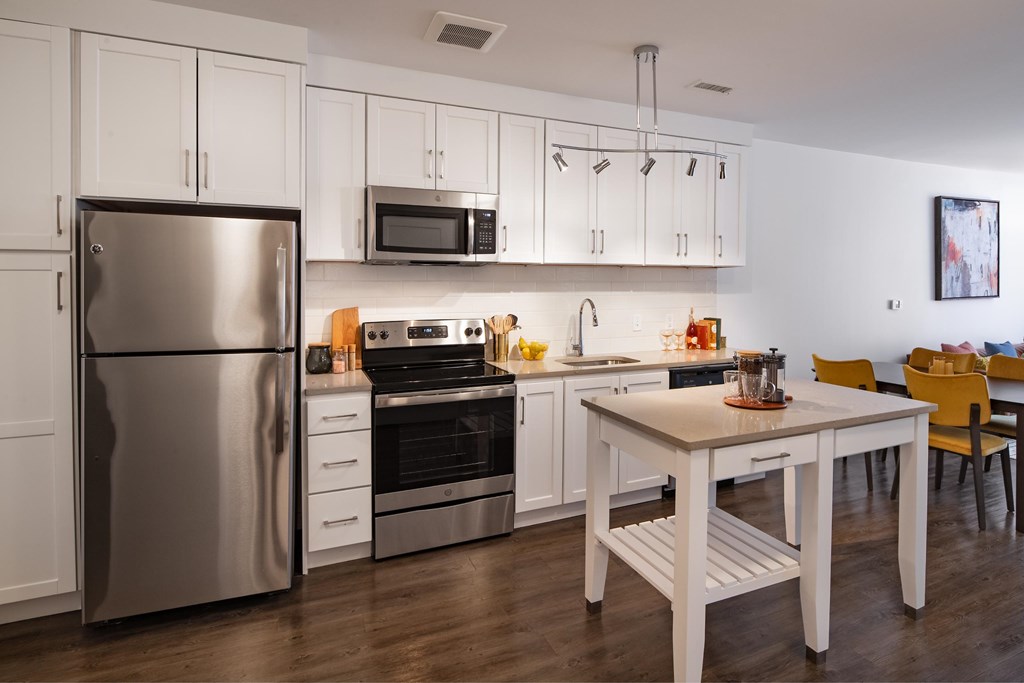 A modern kitchen with a stainless steel refrigerator, microwave, oven, and wooden table.