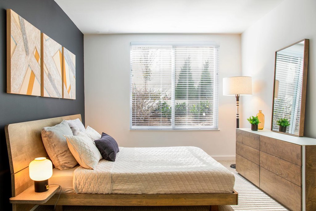 A bedroom with a bed, nightstand, and a window with blinds.