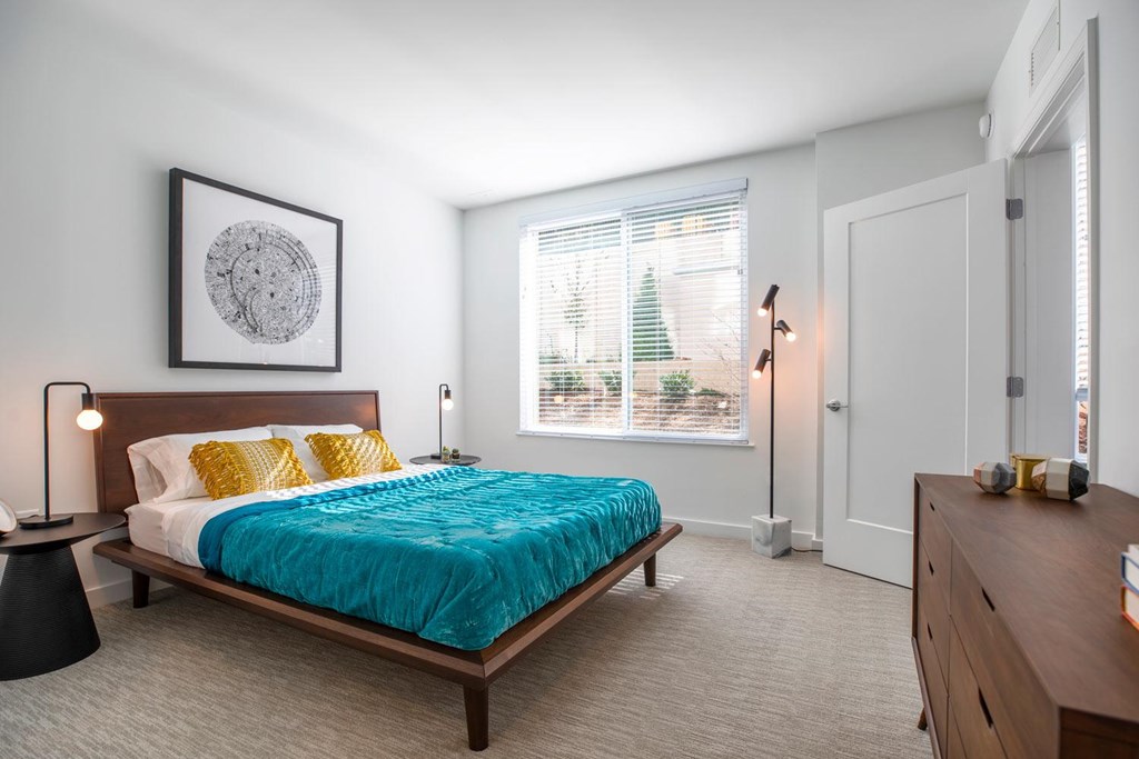A bedroom with a bed, nightstand, and a window with blinds.