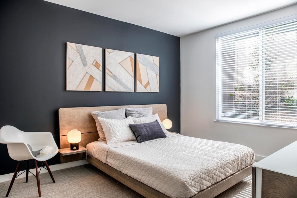 A bedroom with a bed, chair, and a painting on the wall.
