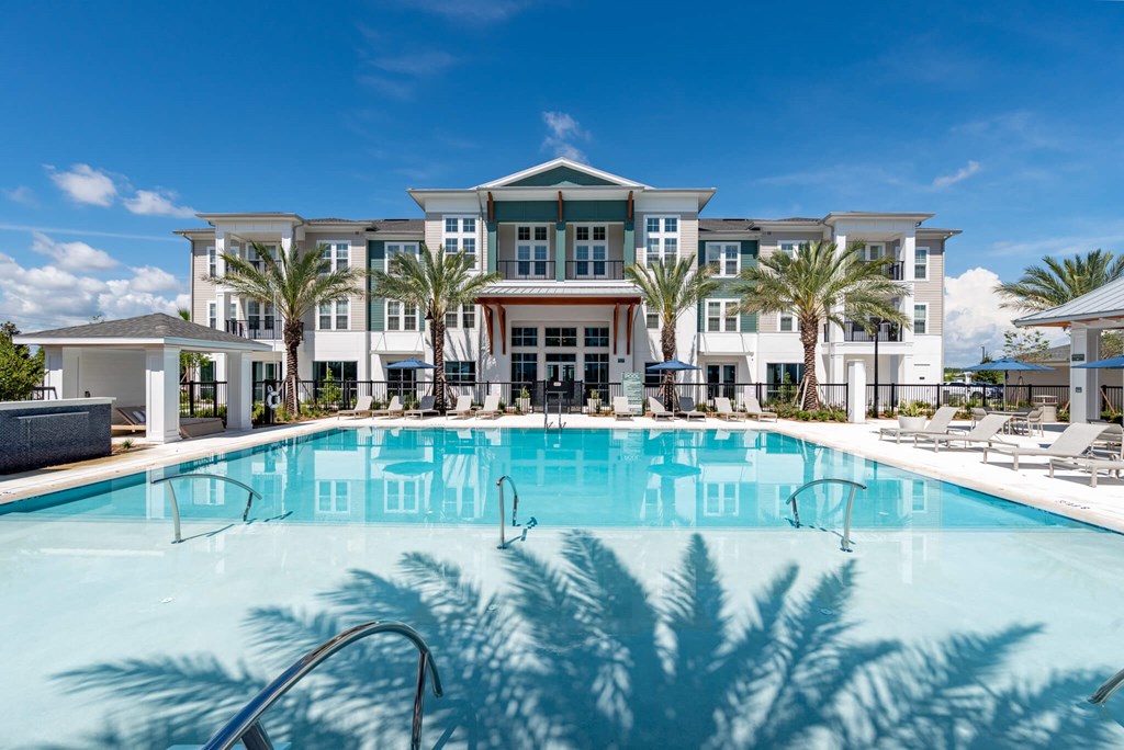 A large swimming pool in front of a multi-story building with palm trees.