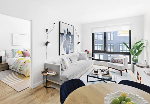 A modern living room with a white sofa, a grey armchair, a wooden coffee table, and a painting on the wall.