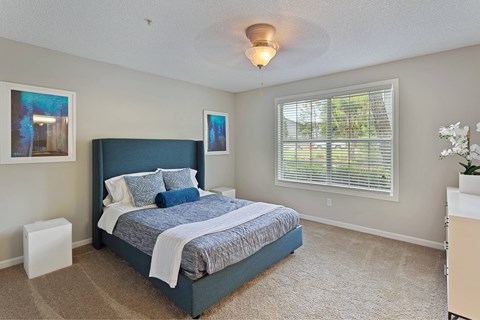 A bedroom with a large bed and a window with blinds.