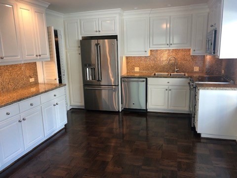 A kitchen with white cabinets and a stainless steel refrigerator.