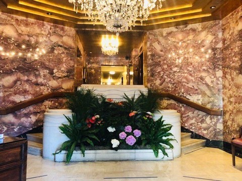 A large floral arrangement sits on a white planter in a marble hallway.