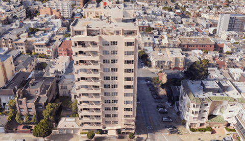 A tall building with a flat roof is surrounded by other buildings.