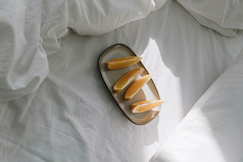 A pair of sandals with orange straps is placed on a white bedsheet.