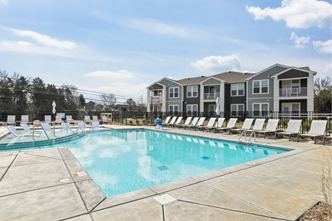 A large swimming pool in front of a building with lounge chairs around it.