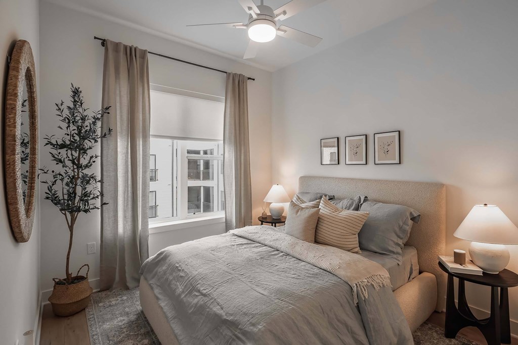 A bedroom with a large bed, a ceiling fan, and a window with curtains.