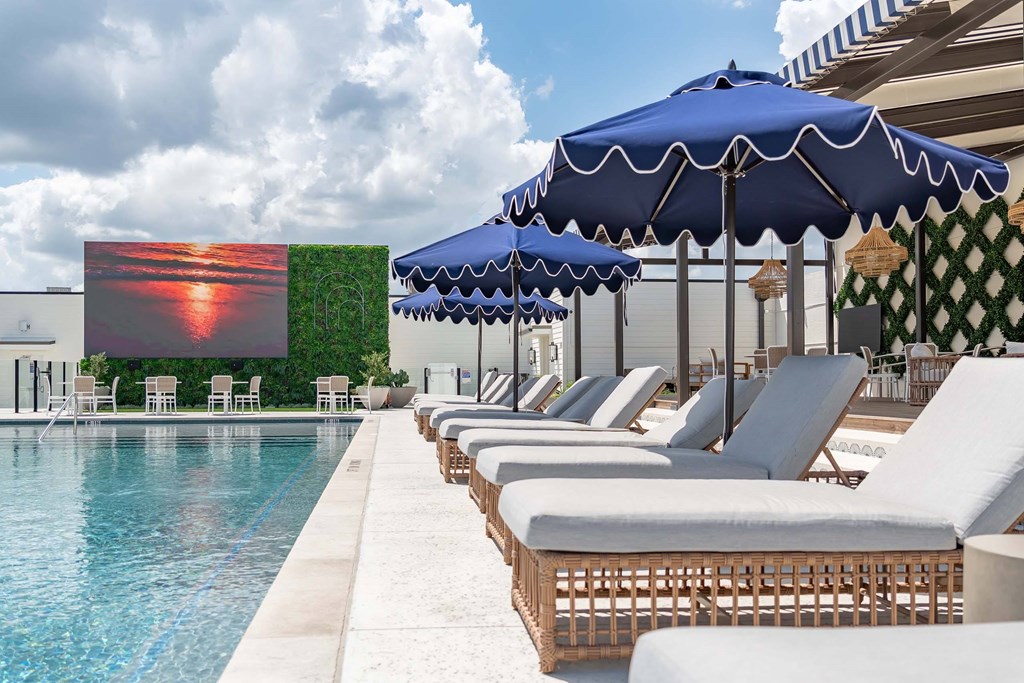 A poolside lounge area with white chairs and blue umbrellas.