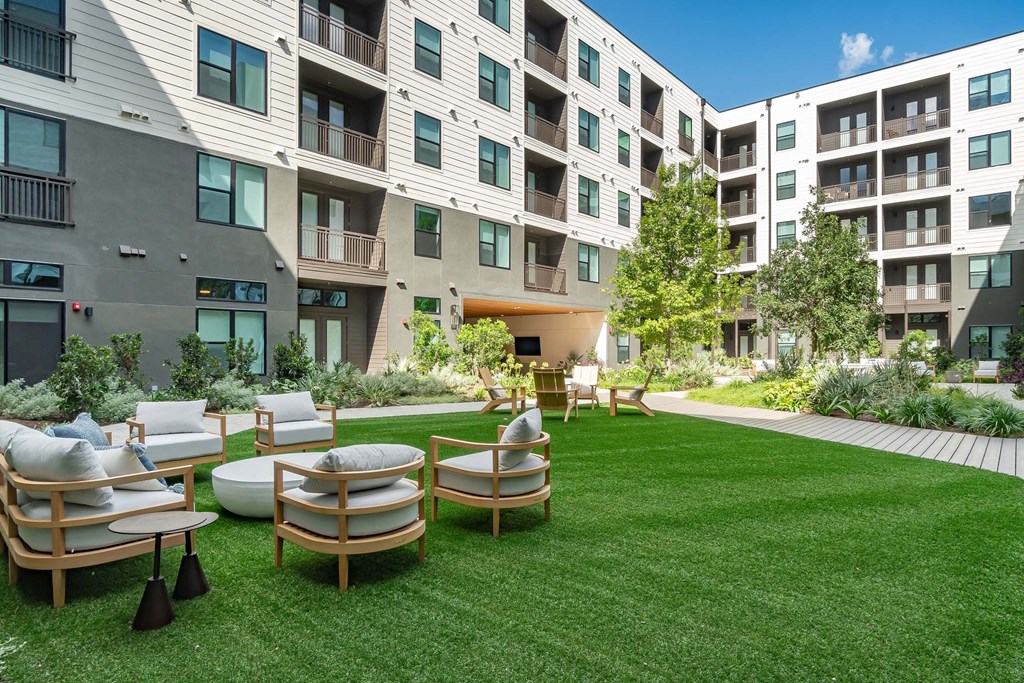 A modern apartment complex with a green lawn and wooden furniture.