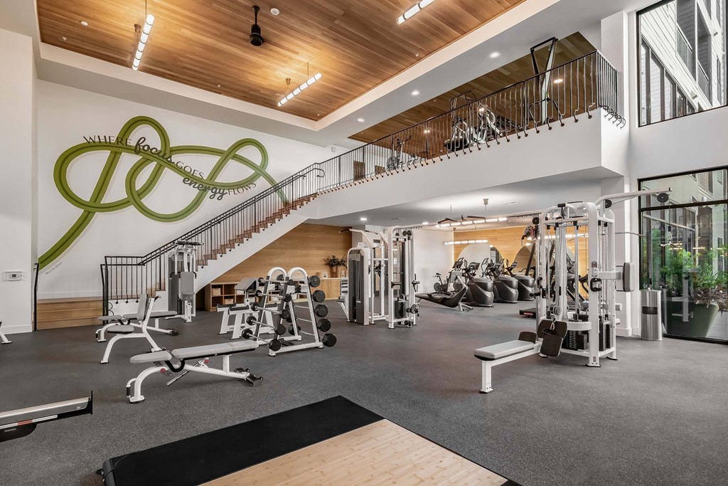 A gym with a variety of equipment and a staircase with a green design on the wall.