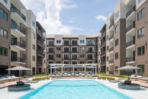 A large swimming pool surrounded by apartment buildings and lounge chairs.