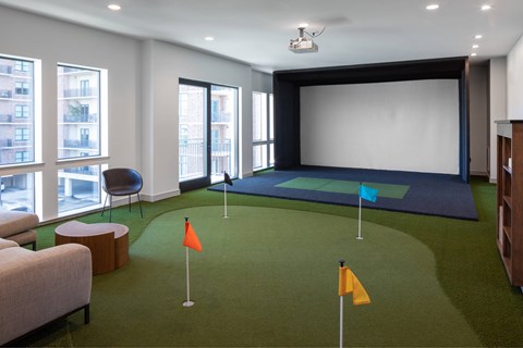 A room with a golf putting green and a large screen.
