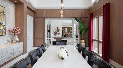 A long table with a white flower centerpiece is surrounded by black chairs in a room with wooden walls.