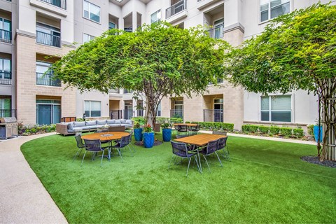 A large grassy area with a table and chairs in front of apartment buildings.